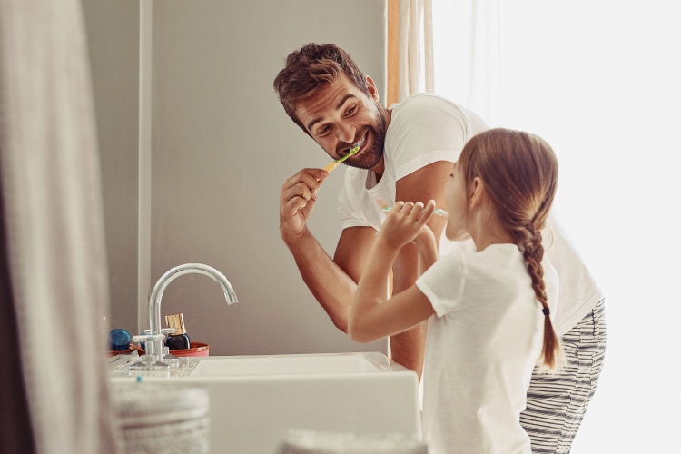 Side view of a dad & daughter brushing their teeth together over a sink
