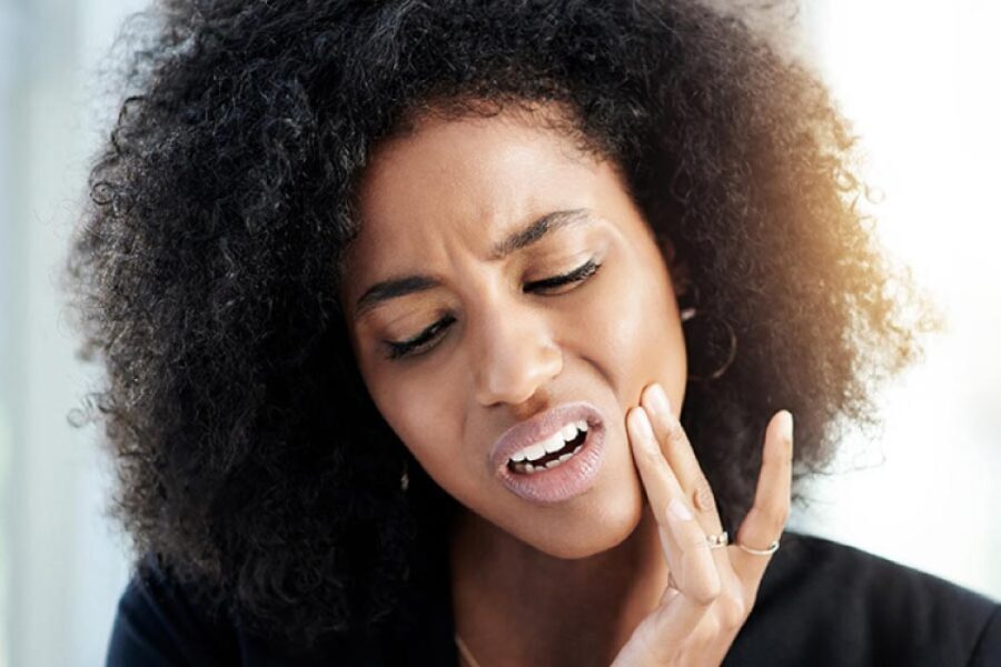 Brown skinned woman with dark curly hair with her fingers to her cheek indicating a toothache.