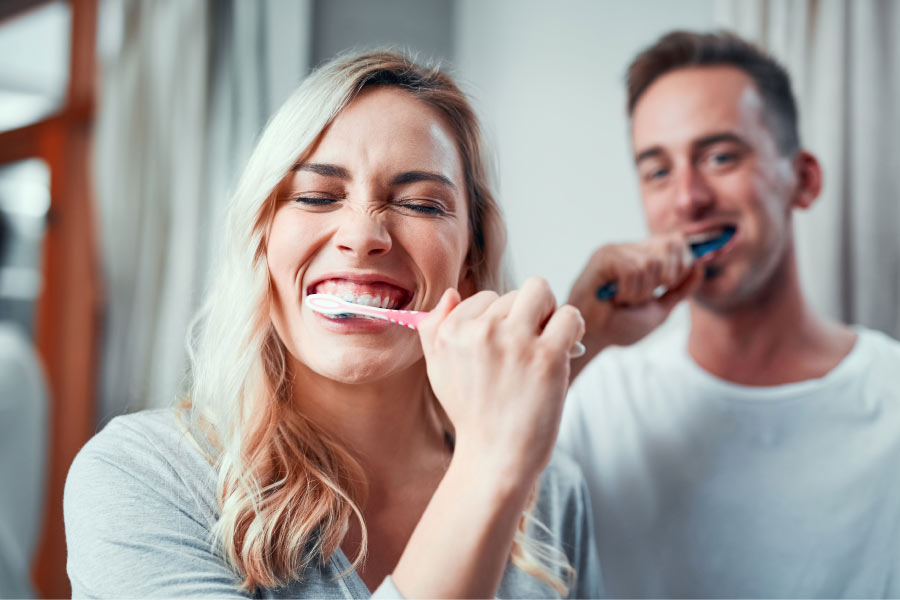 couple brush their teeth together to maintain professional whitening treatments.